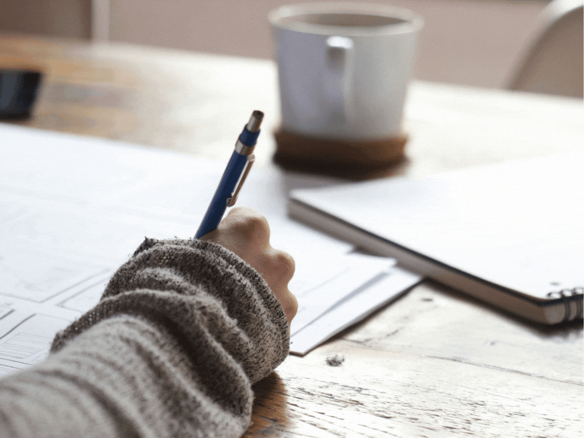 person writing on a piece of paper with a hexagon in HubSpot orange overlaid.